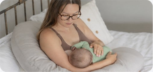 A mother feeding her baby with a pillow supporting her arms.