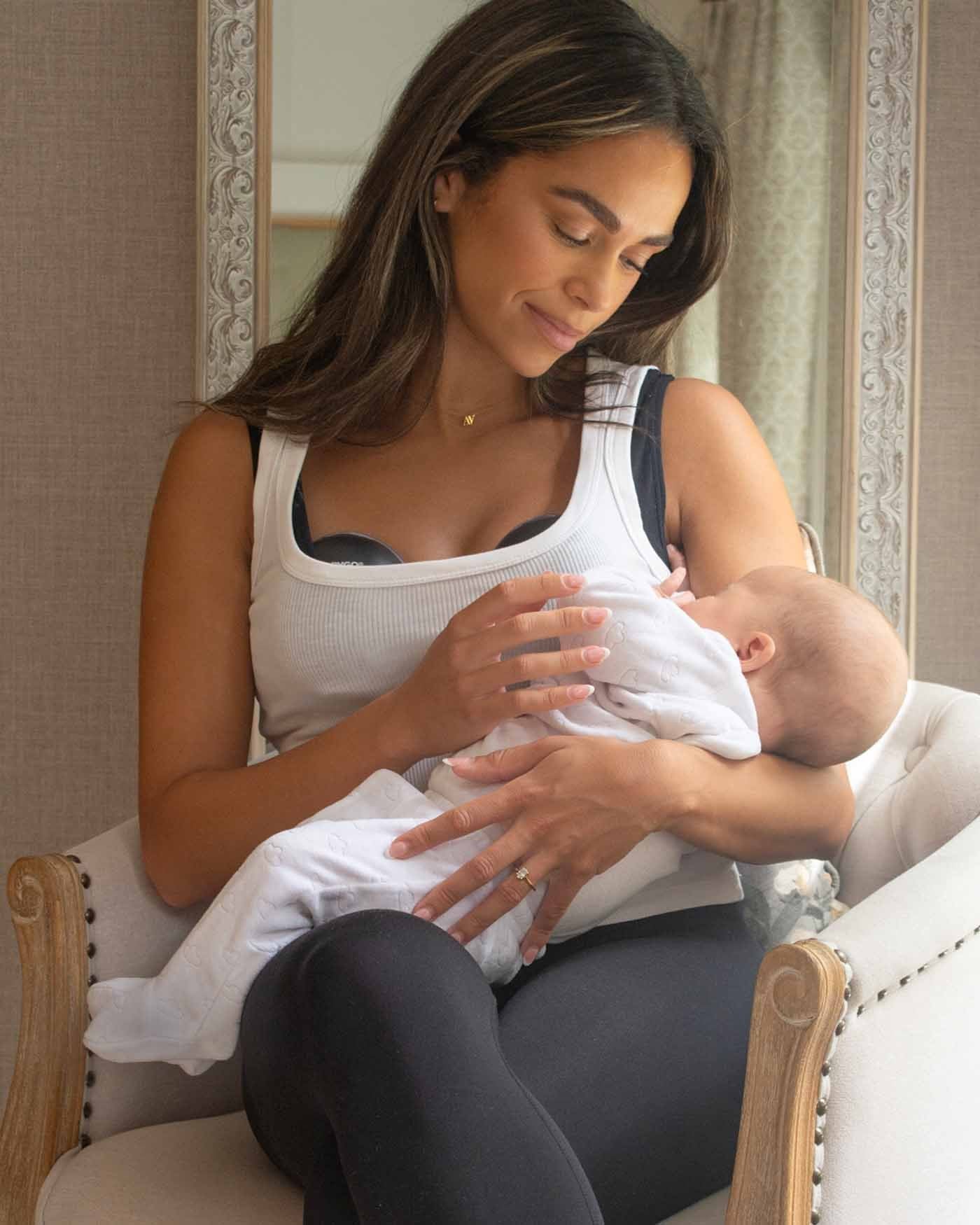 A mother holding her baby in an armchair while wearing the Air pump.