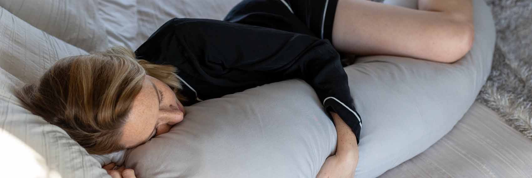 A woman asleep on her side on one half of the bed, hugging the grey pillow.
