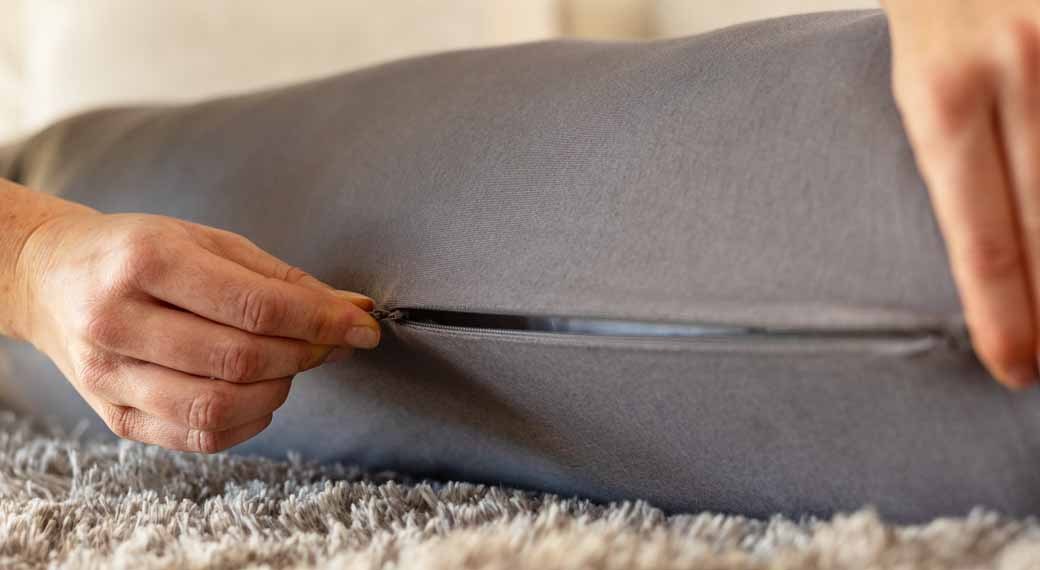 Fingers opening the invisible zip along the grey pillow cover.