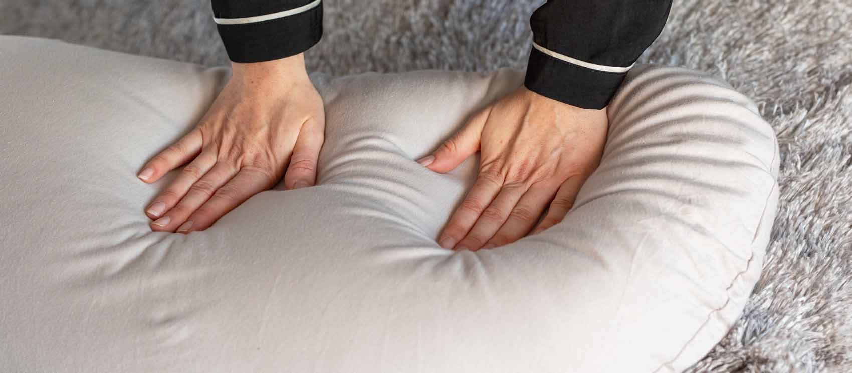Two hands pressing into the oatmeal pillow on a bed.