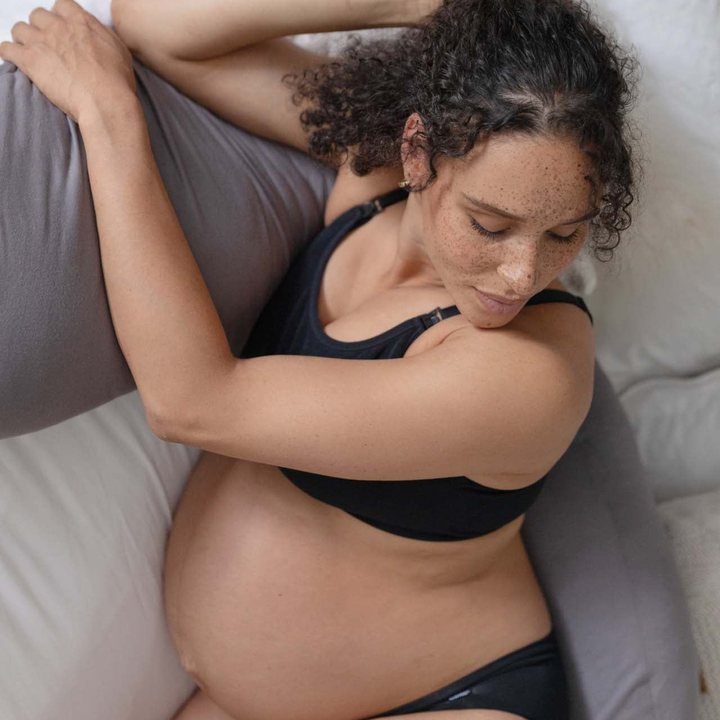 A pregnant woman resting with the grey pillow.